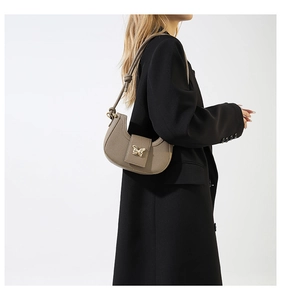 Detail of a beige crescent bag with a gold butterfly clasp and knotted shoulder strap