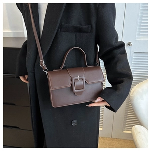 Detail of vintage brown leather handbag on model in black coat showing strap and texture