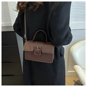 Brown faux leather crossbody bag with square buckle styled on a black wool coat