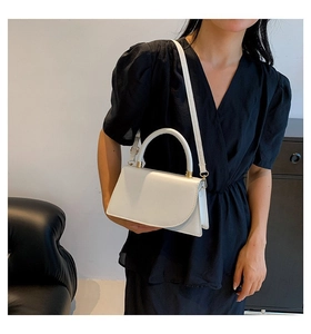 Close-up of a white matte leather crossbody bag featuring gold hardware and curved flap