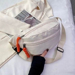 Minimalist beige crossbody bag with vibrant orange zipper pull in a lifestyle scene
