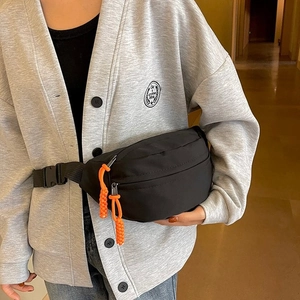Detail of black crossbody chest bag featuring vibrant orange woven zipper pulls and buckle