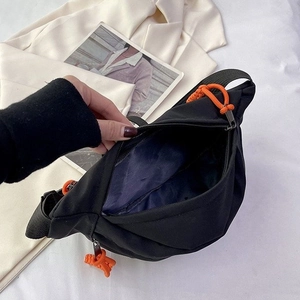 Minimalist black canvas crossbody chest bag with vibrant orange zipper puller detail