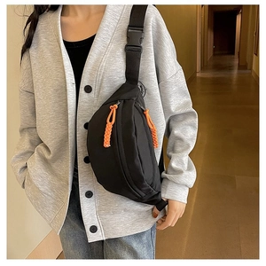 Detail of black nylon sling bag with orange zipper pull cord and adjustable plastic buckle