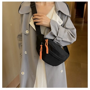 Detail of black nylon sling bag with vibrant orange zipper pulls worn over a gray coat