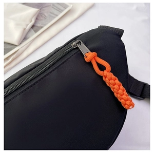 Detail of black sports fanny pack with vibrant orange zipper pulls on fabric