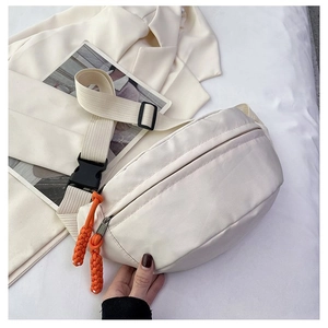 Detail of cream crossbody bag featuring orange woven puller and black buckle closure