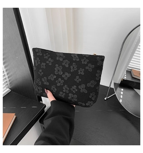 Detalle de neceser jacquard negro con flores y cremallera dorada en la mano