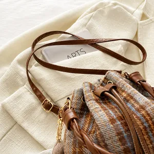Detail of plaid bucket bag featuring braided handle and drawstring closure on blazer