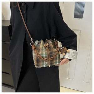Detail der karierten Beuteltasche mit Webgriff und Plüsch-Anhänger auf schwarzem Mantel