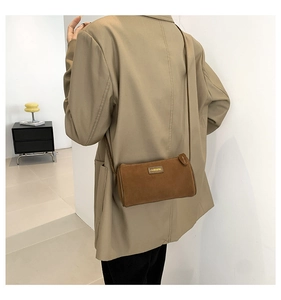 Dettaglio di una borsa a tracolla cilindrica in camoscio marrone con placca logo Hanqing