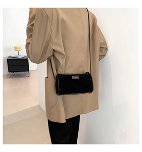 Détail du sac cylindrique en daim noir avec logo doré porté sur un blazer camel chic