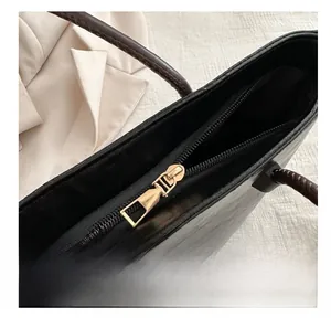 Detail view of a black leather tote bag with a gold metal zipper and woven handle