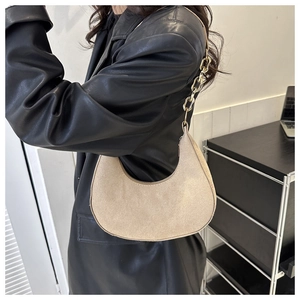 Side view of beige crescent underarm bag with gold chain strap on black leather jacket