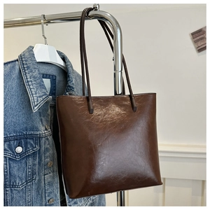 Detail of dark brown glossy leather tote bag hanging on a metal rack with denim jacket