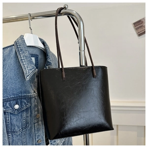 Detail of glossy black leather tote bag with brown straps hanging on a metal rack