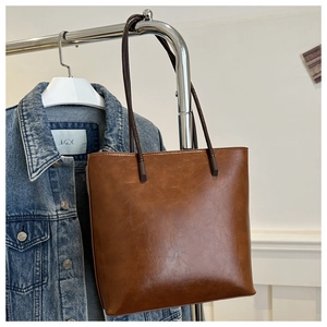 Close-up of brown polished leather tote bag hanging on a rack with denim jacket background