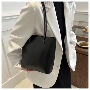 Detail of minimalist black leather tote bag with dark brown straps and matte finish