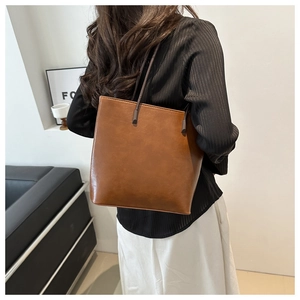 Close-up of a brown minimalist leather tote bag worn by a model in a modern home setting