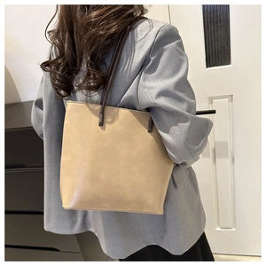 Detailed side view of beige leather tote bag with slim straps worn over a grey blazer