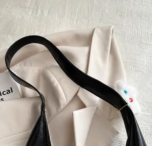 Detail of black tote shoulder strap featuring a cute white plush doll charm accessory