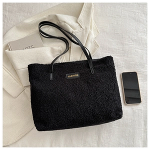 Détail d'un grand sac cabas en peluche noire avec étiquette dorée et anses en cuir