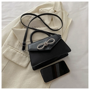 Mini black crossbody bag with silver rhinestone bow shown next to a phone for scale