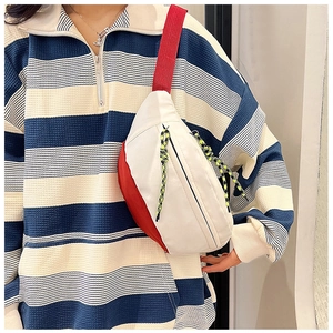 Detail of contrast color crossbody chest bag with woven rope zipper and red accents
