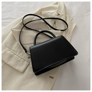 Top view of a black trapezoid leather handbag on a beige textured blazer background