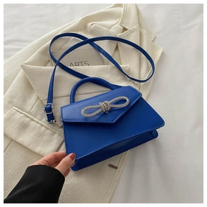 Detail of royal blue trapezoidal bag with silver rhinestone bow on white blazer background