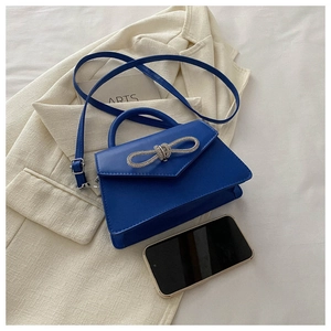 Blue mini handbag with rhinestone bow on beige blazer with a phone for size scale