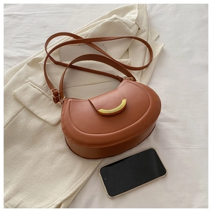 Detail of a brown crescent shoulder bag with golden hardware on a soft fabric background