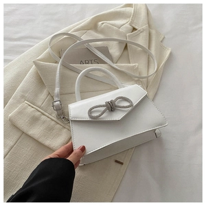 Detail of white crossbody bag with rhinestone bow and matte leather texture on a blazer