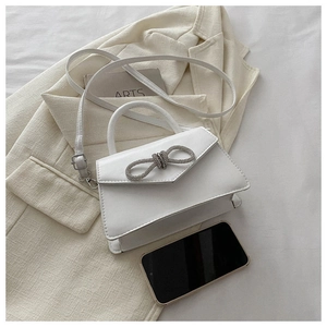 Detail of white mini PU leather handbag with a sparkling bow on a beige blazer