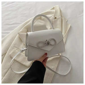 Detail of white leather handbag featuring a sparkling rhinestone bow on the flap cover