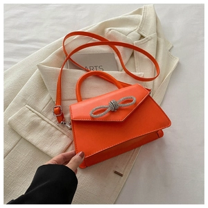 Detail of vivid orange handbag featuring sparkling rhinestone bow and top handle