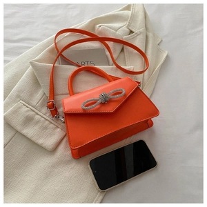 Compact orange crossbody bag with rhinestone bow detail shown next to a smartphone