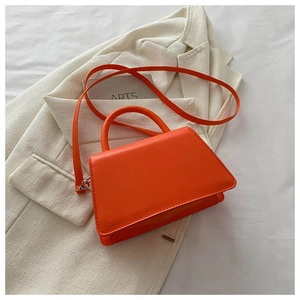 Detail of bright orange faux leather handbag with silver hardware on beige blazer
