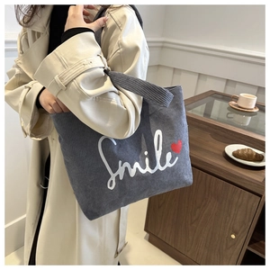 Λεπτομέρεια γκρι κοτλέ τσάντας με τύπωμα Smile σε σκηνικό lifestyle καφετέριας