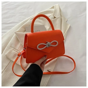 Detail of bright orange handbag featuring a rhinestone bow and elegant stitching