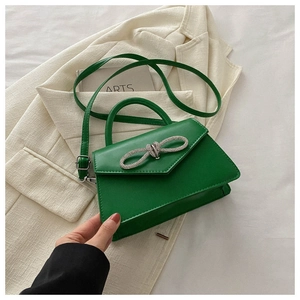 Detail of green leather handbag featuring a sparkling rhinestone bow and triangle flap