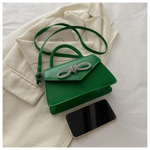 Detail of green leather handbag featuring a sparkling rhinestone bow and silver stitching