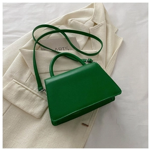 Detail of green trapezoid crossbody bag with silver hardware on a beige blazer