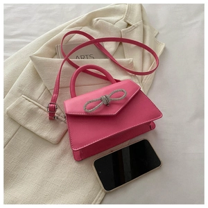 Detail of mini rose pink handbag with rhinestone bow and crossbody strap on blazer