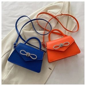 Detail of blue and orange trapezoid bags with rhinestone bow and fine faux leather texture