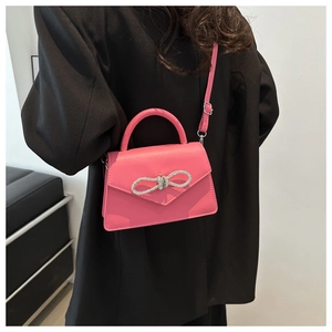Detail of a bright pink crossbody bag with a rhinestone bow buckle on black attire