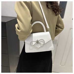 Modern white crossbody bag with rhinestone bow detail shown styled with a green blazer