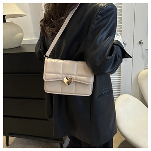 Dettaglio della borsa a tracolla trapuntata beige con chiusura a cuore dorata e finta pelle