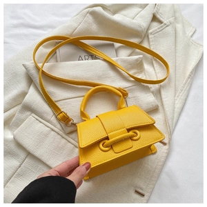Detailansicht der gelben Mini-Handtasche aus Leder mit Litschimuster auf weißem Sakko