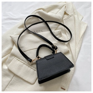 Detail der schwarzen Handtasche mit Litschi-Textur und Gold-Hardware auf beigem Blazer